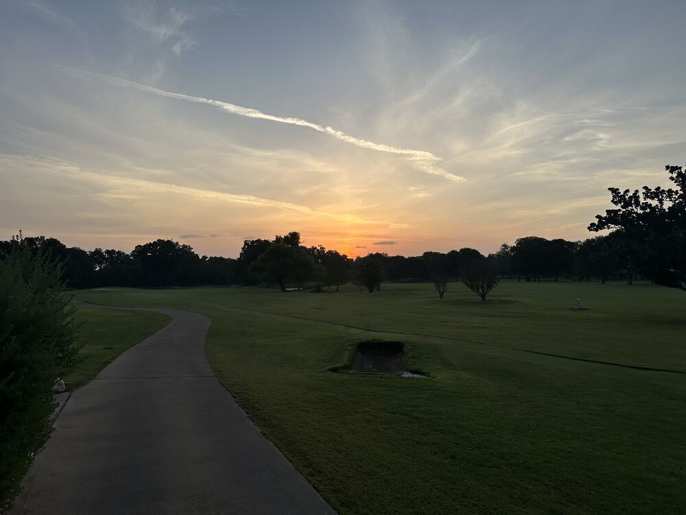 Sunrise breaking orange over the tree line along a cart path on the Onion Creek golf course.